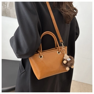 Brown leather bucket bag detail with plush monster charm and fine shoulder strap