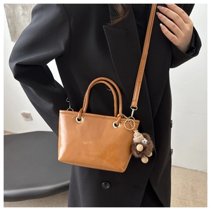 Minimalist caramel brown bucket bag with plush hedgehog charm and shoulder strap