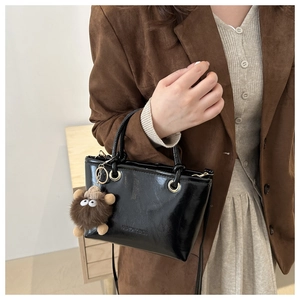 Detail of black glossy leather bucket bag with plush monster charm and fine stitching