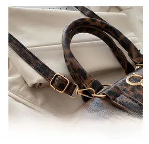 Detailed close-up of leopard print handbag featuring gold metal buckles and adjustable straps