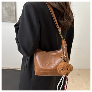 Close-up of brown leather shoulder bag with logo embossing and cute plush puppy charm