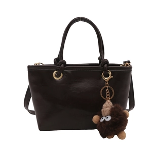 Minimalist chocolate brown leather bucket bag with top handle and plush monster charm