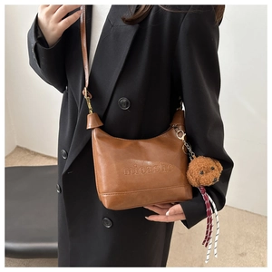 Close-up of brown faux leather shoulder bag with embossed logo and plush puppy charm