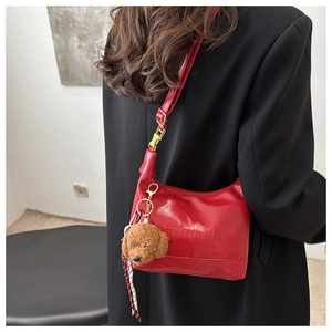 Red leather shoulder bag with embossed logo and teddy bear charm shown on a black blazer