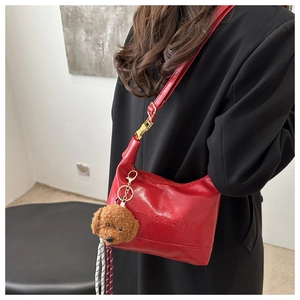 Detail of red glossy PU leather shoulder bag with embossed texture and plush dog charm
