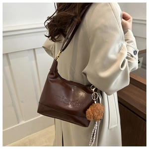 Detail of dark coffee leather handbag with embossed text and plush bear charm on model
