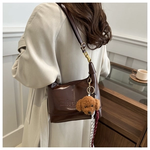 Detail of dark brown glossy leather tote with mioan embossing and teddy bear pendant
