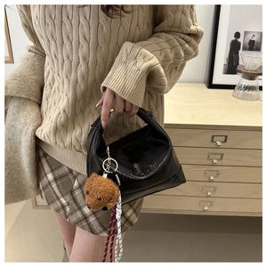 Detail of black leather handbag with embossed texture and a cute brown teddy bear charm