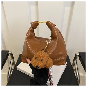 Detail of brown textured tote bag with golden clasp and cute plush dog pendant charm