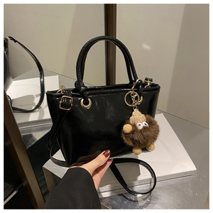 Detail of glossy black patent leather bucket bag with gold ring hardware and plush charm
