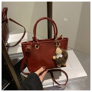 Detail of dark burgundy bucket bag with round handles, gold hardware, and plush charm