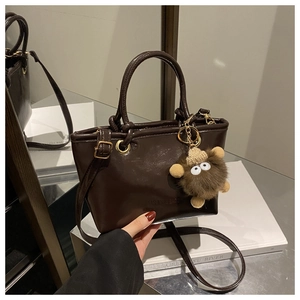 Close-up of a dark brown glossy leather bucket bag with a cute plush monster charm
