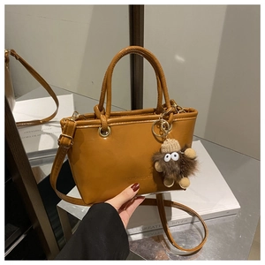 Detail of caramel leather bucket bag with fashion embossing and plush monster charm