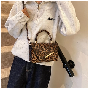 Détail du sac léopard avec finitions dorées et poignée supérieure porté par un mannequin