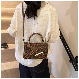 Sac à main chic à motif léopard avec barre dorée porté par un mannequin en vue