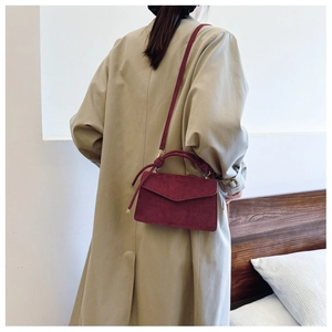 Detail of burgundy matte shoulder bag with decorative knotted handle on trench coat