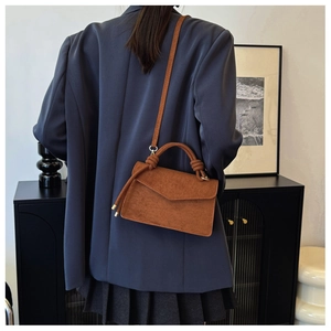 Brown frosted leather mini square bag with unique knotted handle in a stylish indoor setting