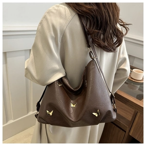 Close-up of deep brown leather tote with golden butterfly charms worn by a model