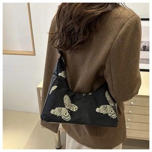 Close-up of black shoulder bag with golden butterfly embroidery and pleated details