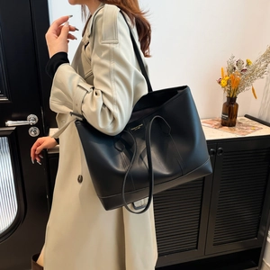 Minimalist black leather tote bag with gold lettering shown on a shoulder for daily commuting