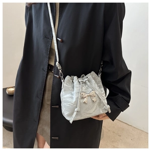 Silver bow-accented drawstring bucket bag with pleated texture and leather strap