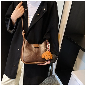Close-up of brown leather shoulder bag with plush puppy pendant and Fashion logo