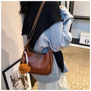 Close-up of vintage brown oil wax leather crescent shoulder bag with a teddy bear charm
