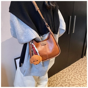 Detail of a brown leather crescent shoulder bag featuring fashion embossing and a cute dog charm