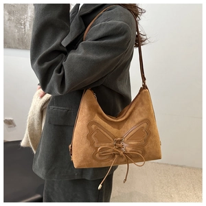 Close-up of brown suede tote bag with leather butterfly appliqué and ribbon details