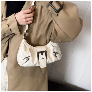 Detailed view of a cream beige faux leather crescent bag with decorative strap and buckles