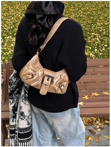 Close-up of khaki pleated leather hobo bag with vintage metal buckles in autumn park