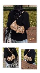 Detail of tan half-moon shoulder bag with retro metal buckles and textured leather finish