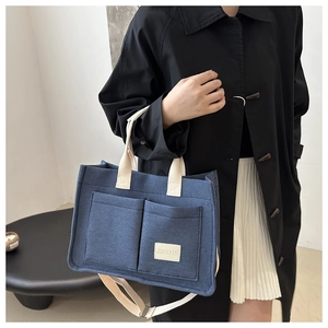 Detail of blue canvas tote bag featuring dual front pockets and adjustable cream strap
