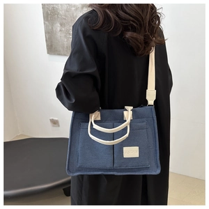 Detail view of large canvas tote bag with front pockets and beige straps on a model