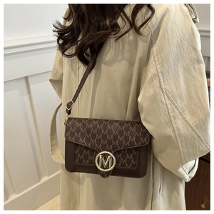 Borsa a tracolla marrone caffè con monogramma M e fibbia logo dorata indossata su un trench-coat