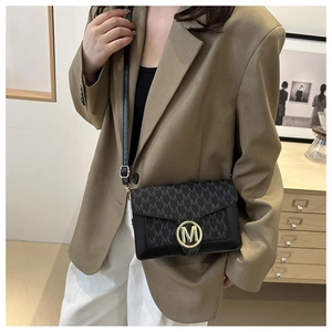 Dettaglio della trama in pelle nera con fibbia dorata a forma di M sulla borsa da donna