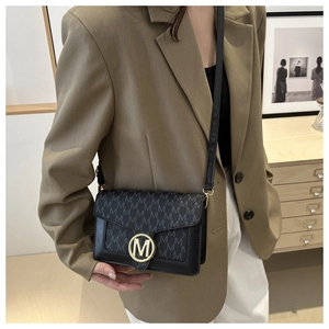 Dettaglio di una borsa a tracolla chic in pelle nera con stampa M e fibbia dorata