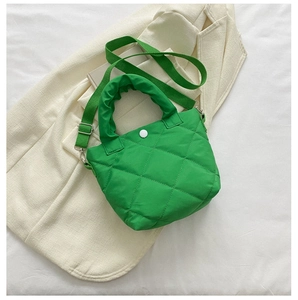 Close-up of bright green quilted bucket bag with ruffles handle on a white blazer
