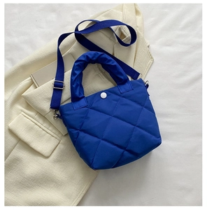 Detail of navy blue quilted bucket bag with ruffly handle on white fabric background
