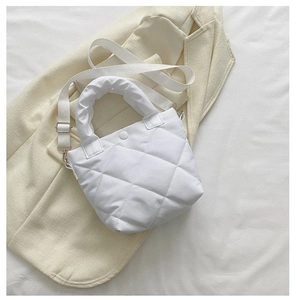 Detail of white quilted bucket bag featuring a soft handle and adjustable strap on a blazer