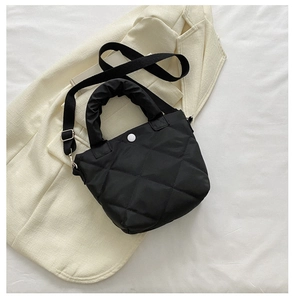 Detail of black quilted puffer bag with cloud-shaped handle on beige blazer
