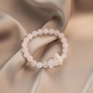 Rosa Quarz Armband mit Bärenanhänger auf elegantem Champagner-Satin Hintergrund