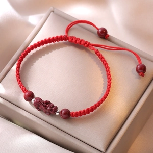 Macro shot of red hand-woven Pixiu bracelet with cinnabar charm and silver beads