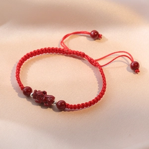 Red braided rope bracelet with cinnabar piyao charm and silver beads on silk background