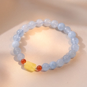 Translucent icy blue aquamarine bead bracelet with amber accents on silk background