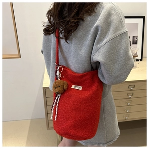 Detail of red woolen bucket bag with teddy bear charm and striped ribbon accent