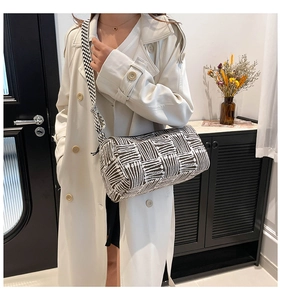 Detail of checkered cylinder crossbody bag with wide woven strap on female model