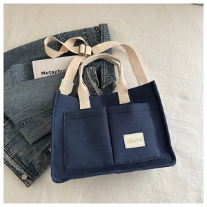 Navy canvas tote bag with front pockets and adjustable strap on white background