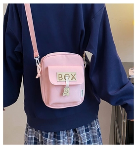 Detail of pink canvas crossbody bag featuring adjustable strap and bear pendant detail