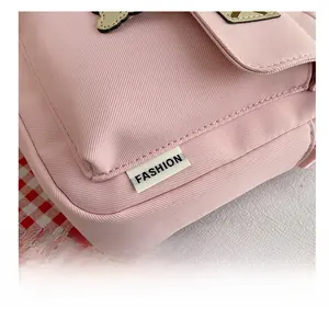 Detail view of pink fabric crossbody bag featuring a stitched black and white FASHION tag